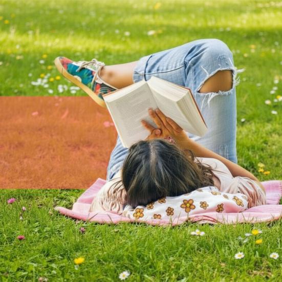 Læsesituation udendørs: Person slapper af i en park og læser en bog på en solrig græsplæne.